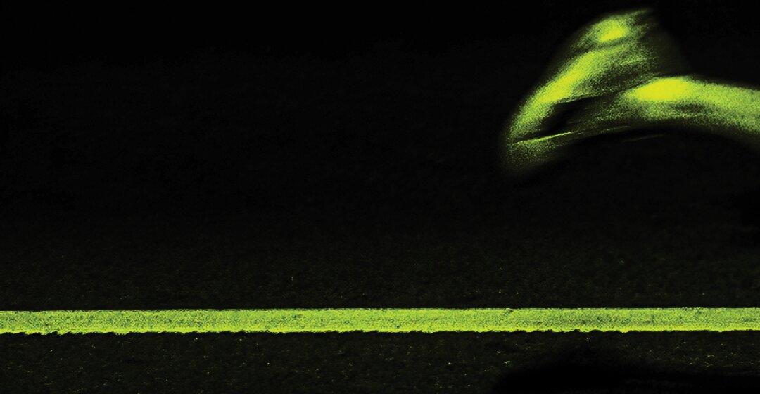 A lane line across night asphalt with one runner's foot blurred by motion above it